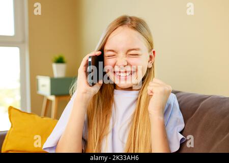 surprised and happy little girl listen great news by phone in cozy living room at home Stock Photo