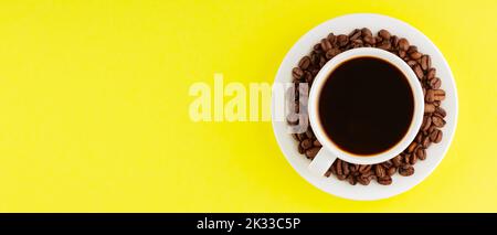 Cup of coffee with coffee beans on yellow background. Black coffee for breakfast. Panoramic shot. Top view Stock Photo