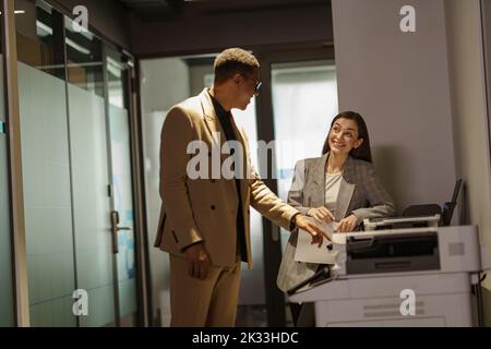 Two business people are talking while scanning documents on a scanner Stock Photo