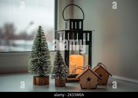 a large chandelier with candles, Christmas trees and wooden houses on the windowsill Stock Photo