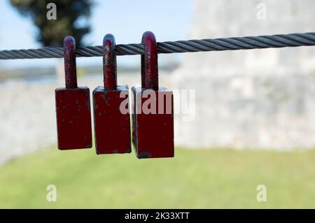 Old and rusty red love padlocks locked on the steel cable, symbol of eternal love Stock Photo