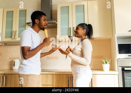 hispanic couple singing together holding a ladle like a microphone in the kitchen Stock Photo