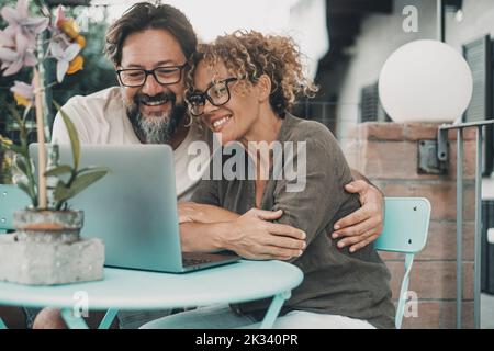 One couple middle age enjoy and have fun together using laptop sitting outdoor at the table in the garden at home. Man and woman in love and friendshi Stock Photo
