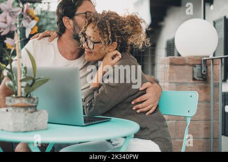 Love and smart modern lifestyle people concept. Man and woman using together a laptop computer outdoor sitting at the table in the garden. Happy coupl Stock Photo