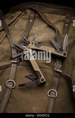 Modern multitool with many tools. A portable multitasking tool on a vintage canvas backpack. Dark background. Stock Photo