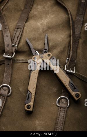 Modern multitool with many tools. A portable multitasking tool on a vintage canvas backpack. Dark background. Stock Photo