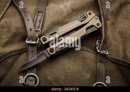 Modern multitool with many tools. A portable multitasking tool on a vintage canvas backpack. Dark background. Stock Photo