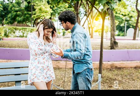 Man and woman arguing in a park. Young couple arguing misunderstanding in a park, Unhappy couple standing arguing in a park. Disgusted teenage couple Stock Photo