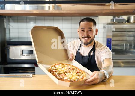 Joyful young cook posing with the pizza he made Stock Photo