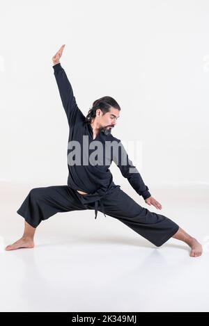 A man dressed in black doing yoga over white background. Studio shot Stock Photo