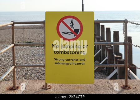 A yellow sign by the sea prohibiting jumping or tombstoning due to strong currents and submerged hazards Stock Photo
