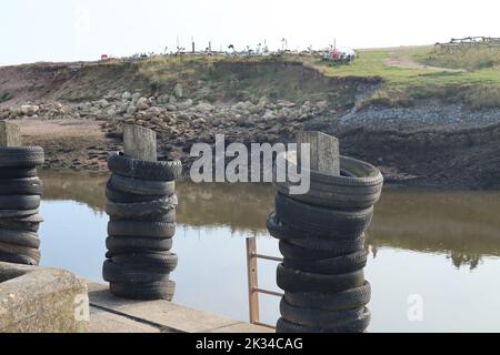Old rubber tyres stacked up on wooden posts at a mooring spot on the river Axe in Axmouth. The tyres prevent damage to the boats. Stock Photo