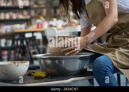 Craftswoman sits at the potter wheel and forms clay vase Stock Photo