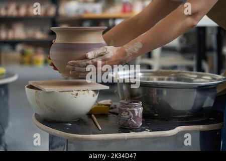 Potter sits his workplace and holds earthen jug in his hands Stock Photo