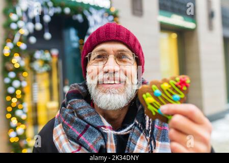happy man showing green sweet cookie christmas tree shape outdoors in winter market Stock Photo