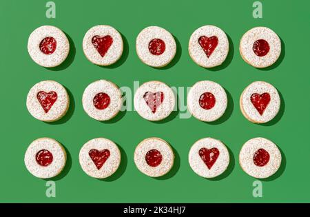 Above view with homemade linzer cookies aligned symmetrically on a green table. Traditional christmas sweets, linzer cookies with raspberry jam. Stock Photo