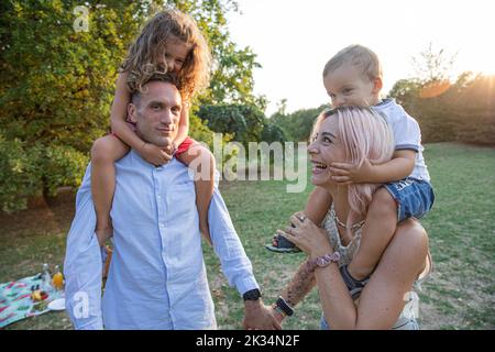 Babies on shoulders and hand in hand, young couple goes for a walk in the park. Stock Photo
