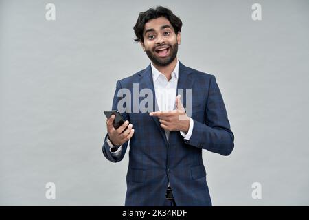 Excited indian business man pointing at mobile phone isolated on beige. Stock Photo