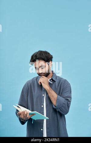 Thoughtful young arab man student writing in notebook isolated on blue. Stock Photo