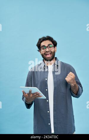 Excited arab man winner raising fistusing tablet isolated on blue. Stock Photo