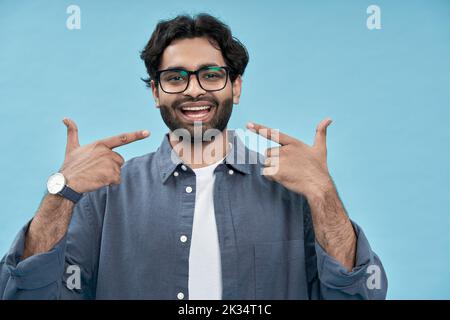 Happy arab man pointing fingers at healthy white teeth isolated on blue. Stock Photo