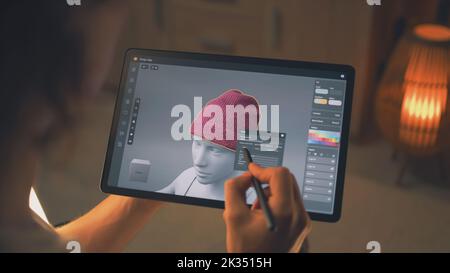 Young male 3D designer working remotely on 3D visualization of clothes in design app using digital tablet computer and stylus Stock Photo