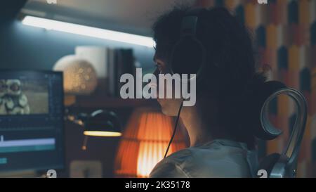 Man in headset editing video with astronauts for client in program on personal computer while working at the table from home at night Stock Photo