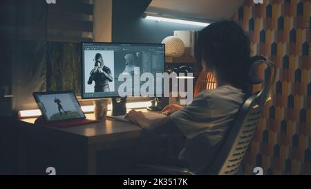 Male 3D designer sitting at the table at home and making animation for video game character, using modern computer and software for creating 3D modeling projects Stock Photo
