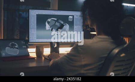 Male young freelancer working from home and creating 3D prototype of modern VR goggles in professional 3D modeling software using pc and digital tablet Stock Photo