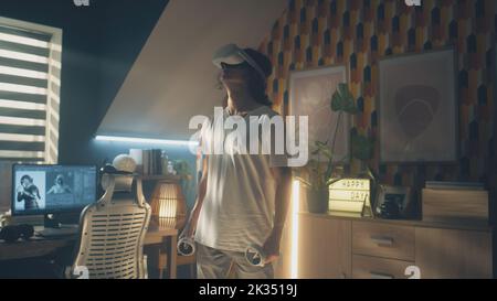Man playing video game using modern VR headset and wireless controllers in leisure time in his room. Virtual reality device. Cyberspace and metaverse Stock Photo