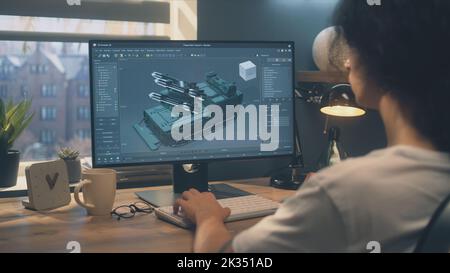 Male 3D designer working on 3D modeling project of house and making exterior in professional computer program, using pc while sitting at the table at home in the evening. Stock Photo