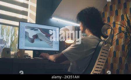 Young guy creating 3D prototype of guitar using modern personal computer and 3D modeling program while working remotely from home Stock Photo