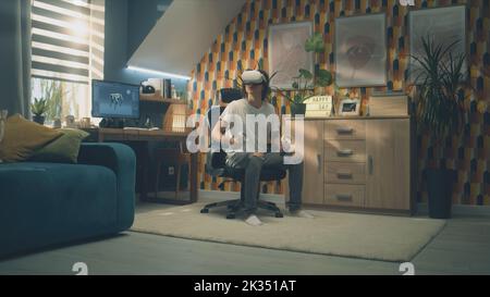 Man playing video game using modern VR headset and wireless controllers in leisure time in his room. Virtual reality device. Cyberspace and metaverse Stock Photo