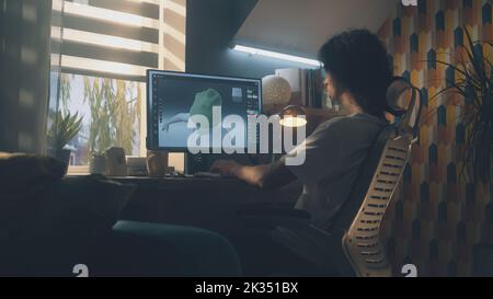 Guy sitting at the table and designing clothes in 3D modeling professional program on personal computer while working remotely from home Stock Photo