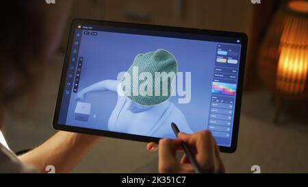 Young male 3D designer working remotely on 3D visualization of clothes in design app using digital tablet computer and stylus Stock Photo