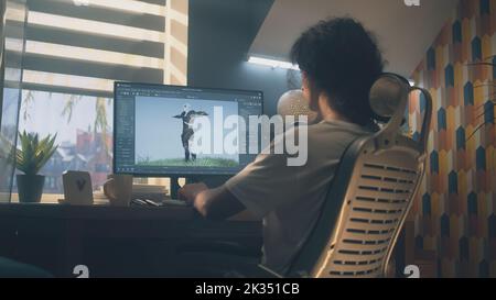 Male 3D designer sitting at the table at home and making animation for video game character, using modern computer and software for creating 3D modeling projects Stock Photo