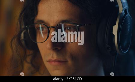 Guy in headphones and glasses at home surfing the internet on computer in spare time and listening to music or working on project remotely Stock Photo