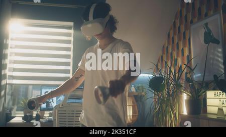 Man testing and playing video game using VR goggles and wireless controllers while spending leisure time at home. Virtual reality device. Cyberspace and metaverse Stock Photo