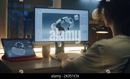 Male young freelancer working from home and creating 3D prototype of modern VR goggles in professional 3D modeling software using pc and digital tablet Stock Photo