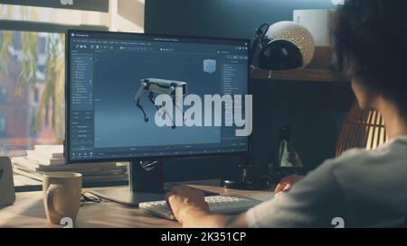 Man sitting at the table and creating 3D prototype of modern robot while working on pc in 3D modeling program remotely from home office Stock Photo
