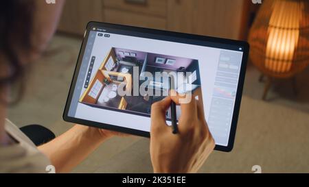 Male 3D designer using digital tablet computer and pencil and creating interior of house in professional design application while working on project remotely Stock Photo