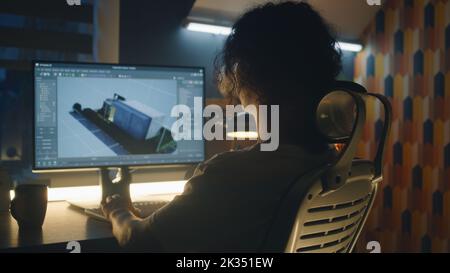 Male 3D designer working on 3D modeling project of house and making exterior in professional computer program, using pc while sitting at the table at home in the evening. Stock Photo