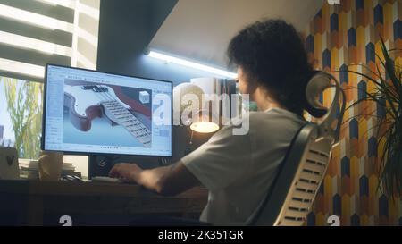Young guy creating 3D prototype of guitar using modern personal computer and 3D modeling program while working remotely from home Stock Photo