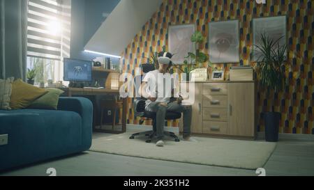 Man playing video game using modern VR headset and wireless controllers in leisure time in his room. Virtual reality device. Cyberspace and metaverse Stock Photo