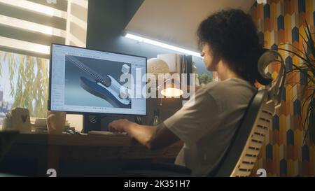 Young guy creating 3D prototype of guitar using modern personal computer and 3D modeling program while working remotely from home Stock Photo