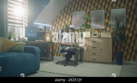 Man playing video game using modern VR headset and wireless controllers in leisure time in his room. Virtual reality device. Cyberspace and metaverse Stock Photo