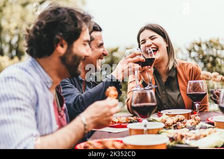 A group of friends meet on the weekend eating grilled meat, laughing, talking carefree and drinking red wine while having fun together - food and drin Stock Photo