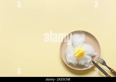 Composition with table setting and sweet cotton candy in shape of fried egg on yellow background Stock Photo