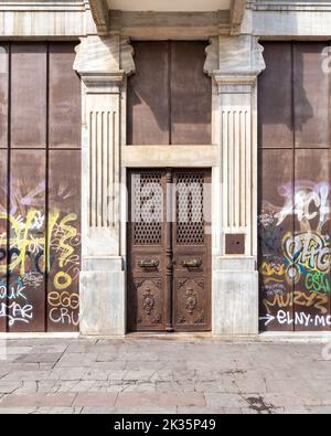 Exterior shot of grunge rusted metal door mediating two marble columns in an abandoned building on city street Stock Photo