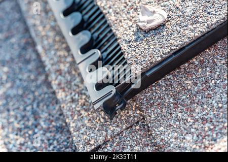 Ridge cap vent installed on a shingle roof for passive attic ventilation on a residential house.  Stock Photo